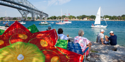 People sitting under a colorful umbrella watching sailboats race in the Mackinac Race