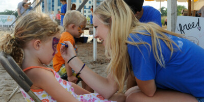 A woman painting the face of a girl on the beach at Grand Bend