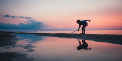 LOCATION: GRAND BEND, ON Child playing on the shore at sunset in Grand Bend
