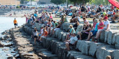 Crowd of people sitting on large rocks along the St. Clair river to watch the Mackinac Race